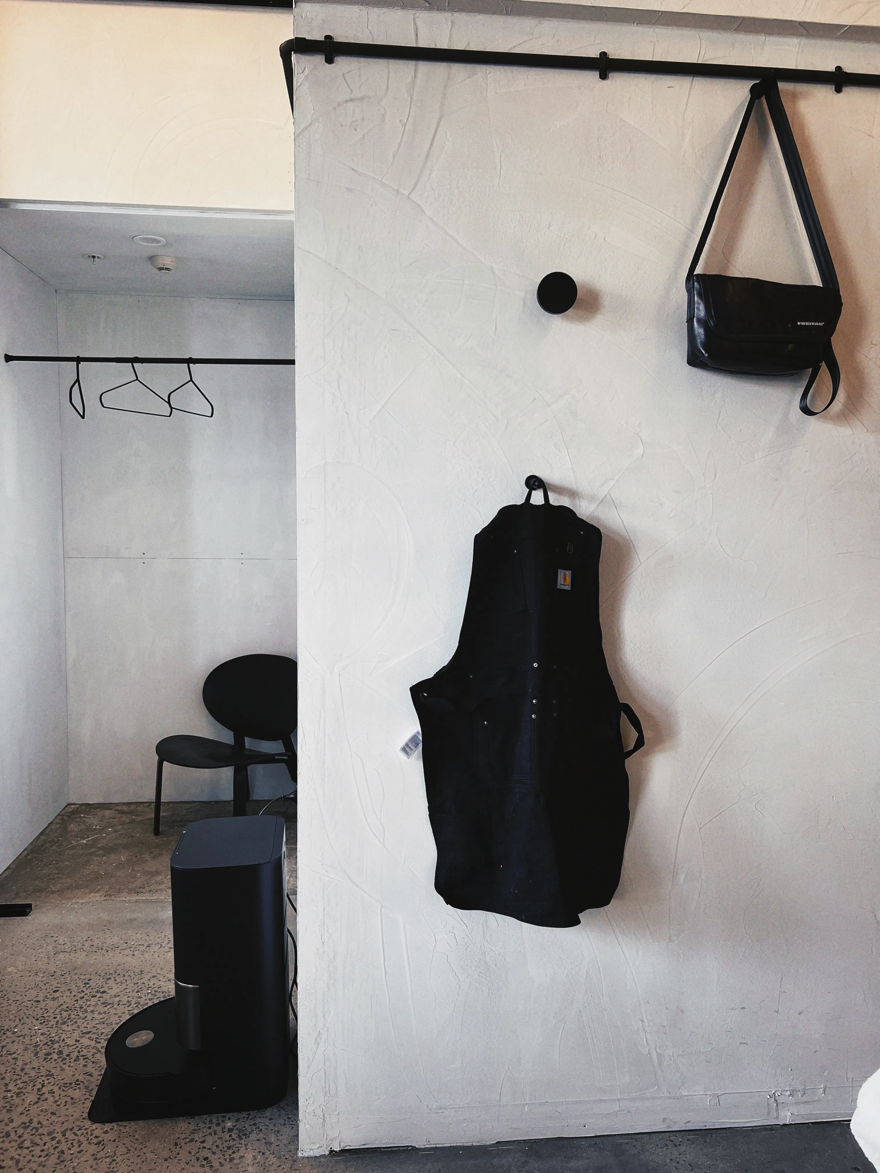 The studio entry — black work apron and bag on a rail against hand-troweled plaster wall